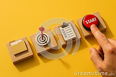 Finger pressing red start button next to checklist, target and folder icons on wooden blocks over yellow background, symbolizing Stock Photo
