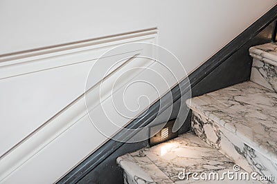 The Junction Of Stone Steps With Built-in Lighting, Baseboards And White Walls With Moldings Stock Photo