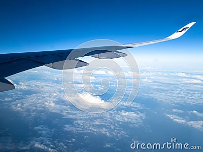 Finnair airplane wing flying in the blue sky with white clouds below Editorial Stock Photo