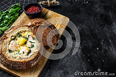Finnish Creamy fish soup with salmon, trout, potatoes served in bread. Black background, top view, space for text Stock Photo