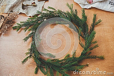 Fir branches circle, thread, berries, herbs on wooden table. Rustic Christmas wreath workshop. Authentic stylish still life. Stock Photo