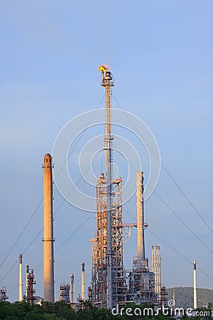 Fire burning over oil refinery chimney against blue sky Stock Photo