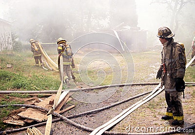 A fire chief watches two fellow firefighters carrying hoses Editorial Stock Photo