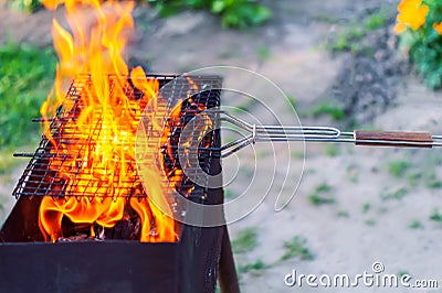 Fire in the grill. The red flames of a campfire blaze through the empty grill grate, burning wood in the backyard grill on the gre Stock Photo