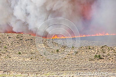 Fire line and dense gray smoke from a large wildfire over a partially burned area in the desert Stock Photo