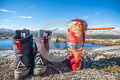 Fire maple Outdoor cookery with propane gas boiler next to Alfa hiking boots with mountain scenery view. Editorial Stock Photo