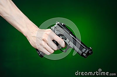 Firearms and murderer topic: human hand holding a gun on a dark green background isolated in studio Stock Photo