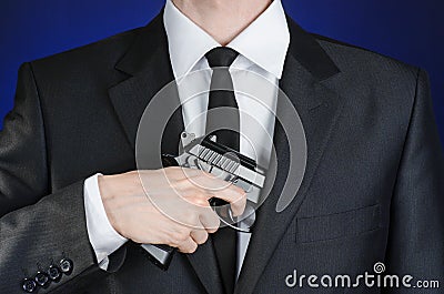 Firearms and security topic: a man in a black suit holding a gun on a dark blue background in studio isolated Stock Photo