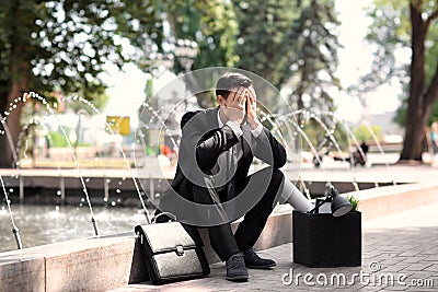 Fired office worker with personal stuff sitting near fountain outdoors Stock Photo