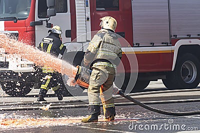 Firefighter - Firemen extinguishing a large blaze, they are standing with protective wear against the background of fire truck Editorial Stock Photo