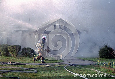 A firefighter walks in front of a building that is onm fire Editorial Stock Photo