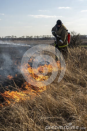 Firefighters extinguish the flames of burning grass Stock Photo