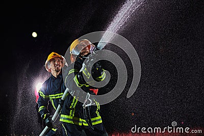 Firefighters using a water hose to eliminate a fire hazard. Team of female and male firemen in dangerous rescue mission Stock Photo