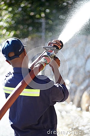 Fireman at work. Rearview shot of a fireman spraying water with a fire hose. Editorial Stock Photo