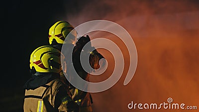 Firemen extinguish fire with the hose. Burning house fire drill. Back view Stock Photo