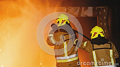 Firemen extinguish fire with the hose. Burning house fire drill. Back view Stock Photo