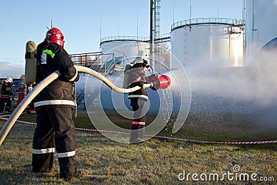 Firemen extinguish fire at oil tanks by foam spraying hose Stock Photo