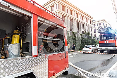 Firemen wearing uniform standing behind fire tape and many fire engine trucks with ladder at accident in highrise tower Editorial Stock Photo