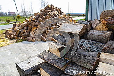 A firewood stacked in a pile, lying on the property near the metal garage, wooden background. Stock Photo