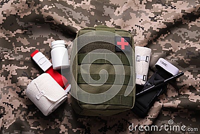 First aid kit with medical tourniquet, pills and bands on military fabric, flat lay Stock Photo