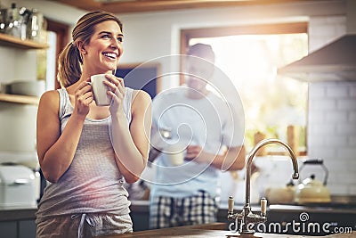 First coffee then everything else. a young woman having her morning coffee with her boyfriend standing in the background Stock Photo