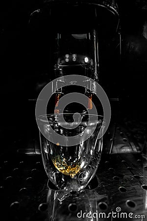 First drops of coffee falling through the double spout into a glass cup with foam and bubbles from an automatic espresso machine Stock Photo