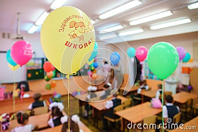 First-form schoolchildren in classroom at school desks on holiday of beginning of elementary school education. Balloons as Editorial Stock Photo