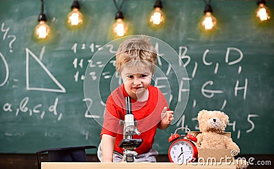 First former interested in studying, learning, education. Kid boy near microscope in classroom, chalkboard on background Stock Photo