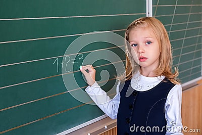 First grade pupil a girl writing on green blackboard at school lesson Stock Photo