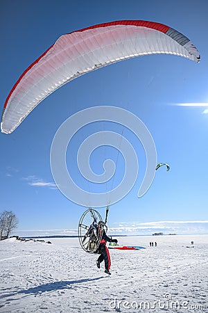 The first moments of taking off a motor paraplane over a large snow covered lake in bright sunny weather Stock Photo