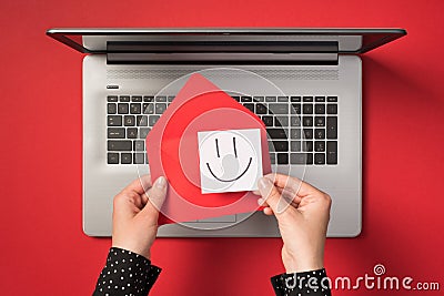 First person top view photo of hands holding red vivid envelope and white sticker note paper with drawn smiling face over open Stock Photo