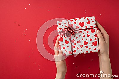 First person top view photo of valentine`s day decor glitter girl`s hands demonstrating gift box in white wrapping paper with Stock Photo