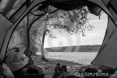 First-person view from the tent. The concept of travel and camping on a motorcycle in the wild. Riverbank, bonfire and motobike. Stock Photo