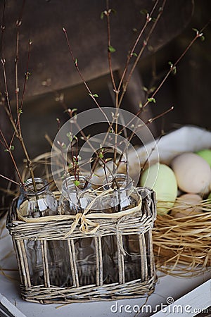 First spring twigs in bottles in basket with easter eggs on background Stock Photo