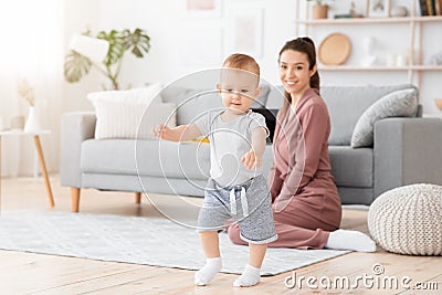 First Steps. Adorable smiling baby boy learning how to walk at home, Stock Photo