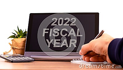 2022 fiscal new year symbol. Tablet with words `fiscal year`. Businessman hand with pen, house plant. Copy space. Beautiful whit Stock Photo