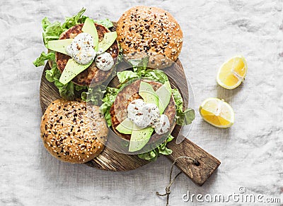 Fish burger. Burgers with tuna, avocado and mustard sauce with whole grain homemade buns on wooden cutting board on a light backgr Stock Photo