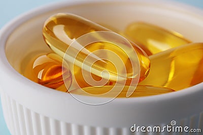 Fish oil. Yellow softgels or capsules are in white bottle cap. Light blue surface. Vitamins and healthy lifestyle. Illustration Stock Photo