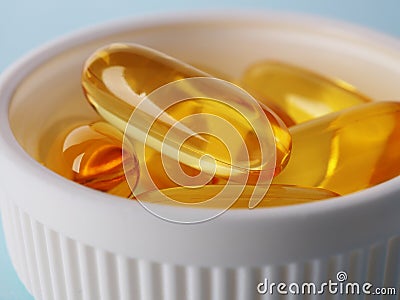 Fish oil. Yellow softgels or capsules are in white bottle cap. Light blue surface. Vitamins and healthy lifestyle. Illustration Stock Photo