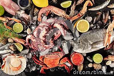 Fish and seafood variety, a flatlay overhead shot on a dark background. Fresh sea bream. shrimps, crab, sardines, squid Stock Photo