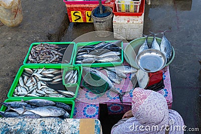 A fish sellers in the jimbaran bali fish market. He sells various types of fresh fish that have just been caughta Muslim woman is Stock Photo
