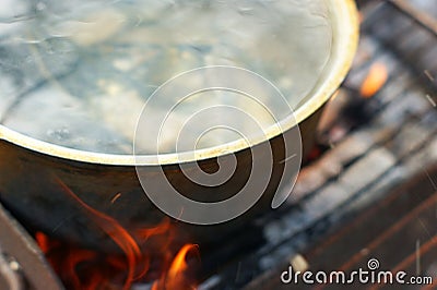 Fish soup with grayling cooked in large castiron pot at bonfire Stock Photo