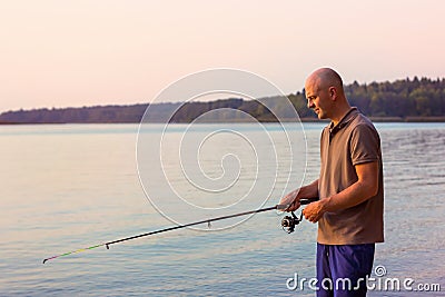 Fisher fishing with spinning rod at sunrise. Stock Photo