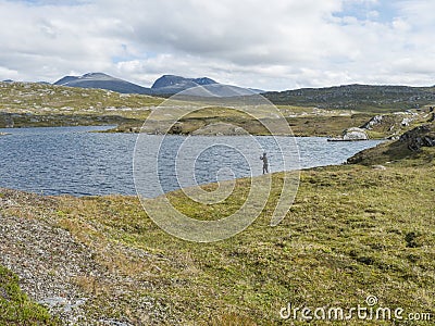 Fisherman, angler figure at northern landscape, tundra in Swedish Lapland with blue artic lake, green hills and Stock Photo