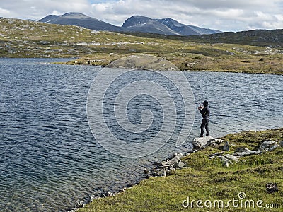 Fisherman, angler figure at northern landscape, tundra in Swedish Lapland with blue artic lake, green hills and Editorial Stock Photo