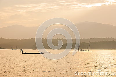 Fisherman on fishing boat in The Sirikit Dam, raft dip net and sunset sky backgrounds. Golden sun setting shines down around the Stock Photo