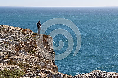 A fisherman with a fishing rod on a high ocean shore on a sunny windy day. Editorial Stock Photo