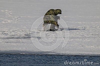 A fisherman sits on thin melting ice and catches fish, not paying attention to the danger of falling through the ice and dying Stock Photo