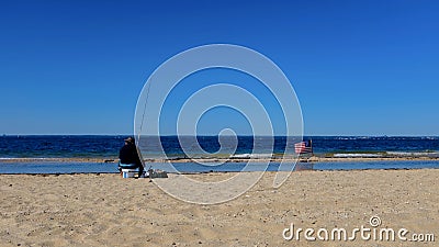 Fisherman Sitting on a Bucket On a Beach with American Flag Nearby with Copy Space Stock Photo