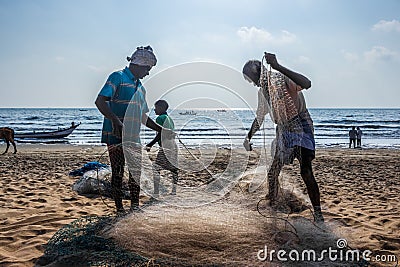 Fisherman taking the fish from Nylon Fishing net. Indian fisherman working on their net on beach sand Editorial Stock Photo